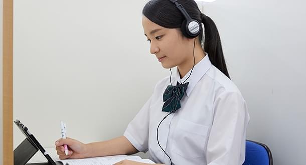 ヘッドフォンで音声を聞きながら勉強する女子学生
